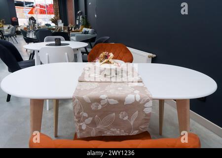 Weißer Holztisch kombiniert mit orangefarbenen Stühlen mit weichen Stoffpolstern. Es gibt eine weiße Lieferung mit einem mehrfarbigen Blumenstrauß auf dem t Stockfoto