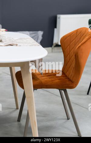 Weißer Holztisch kombiniert mit orangefarbenen Stühlen mit weichen Stoffpolstern. Es gibt eine weiße Lieferung mit einem mehrfarbigen Blumenstrauß auf dem t Stockfoto