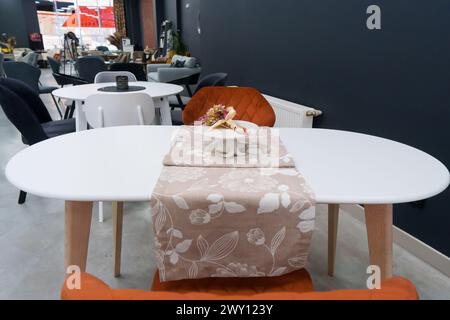 Weißer Holztisch kombiniert mit orangefarbenen Stühlen mit weichen Stoffpolstern. Es gibt eine weiße Lieferung mit einem mehrfarbigen Blumenstrauß auf dem t Stockfoto