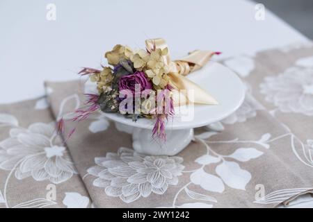 Weißer Holztisch kombiniert mit orangefarbenen Stühlen mit weichen Stoffpolstern. Es gibt eine weiße Lieferung mit einem mehrfarbigen Blumenstrauß auf dem t Stockfoto