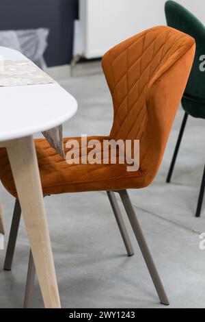 Weißer Holztisch kombiniert mit orangefarbenen Stühlen mit weichen Stoffpolstern. Es gibt eine weiße Lieferung mit einem mehrfarbigen Blumenstrauß auf dem t Stockfoto