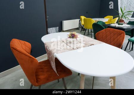 Weißer Holztisch kombiniert mit orangefarbenen Stühlen mit weichen Stoffpolstern. Es gibt eine weiße Lieferung mit einem mehrfarbigen Blumenstrauß auf dem t Stockfoto