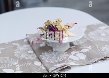 Weißer Holztisch kombiniert mit orangefarbenen Stühlen mit weichen Stoffpolstern. Es gibt eine weiße Lieferung mit einem mehrfarbigen Blumenstrauß auf dem t Stockfoto