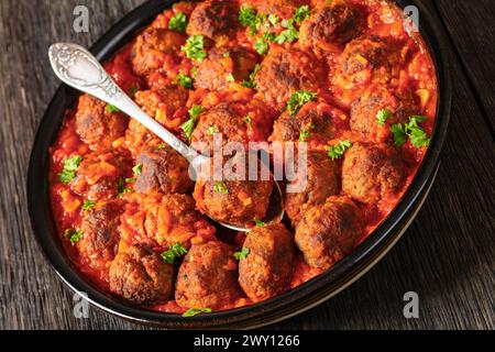 Albondigas, spanische Fleischbällchen aus Schwein und Rindfleisch in Tomatensoße mit roter Paprika, Zwiebelsoße in Backform auf dunklem Eichenholztisch in Nahaufnahme Stockfoto