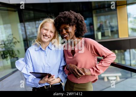 Zwei Frauen mit ähnlichen Merkmalen stehen nebeneinander, lächelnd, vor der großen Architektur. Stockfoto