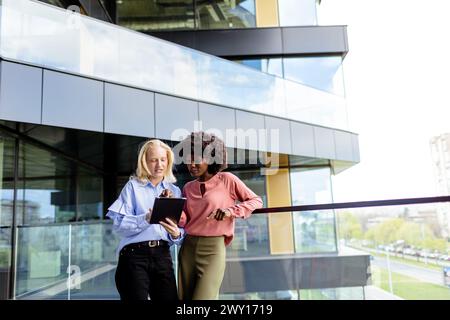 Zwei Frauen mit ähnlichen Merkmalen stehen nebeneinander, lächelnd, vor der großen Architektur. Stockfoto