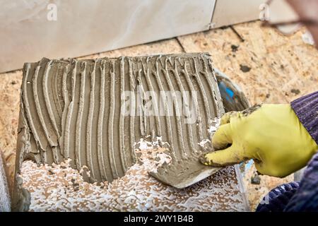 Zementmörtel aus Fliesenkleber wird mit einer gekerbten Kelle auf Fliesen aufgetragen. Stockfoto