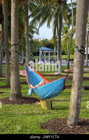 Miami, Florida, USA - 1. Dezember 2023: Person, die in einer Hängematte zwischen Palmen im Park nahe South Pointe am Ende von Miamis South Beach liegt Stockfoto