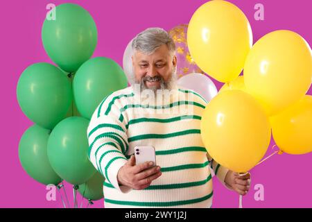 Senior Mann mit Ballons, die Selfie auf rosa Hintergrund machen Stockfoto