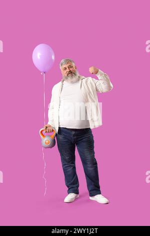 Seniorenmann mit Ballon und Kettlebell, der Muskeln auf rosa Hintergrund zeigt Stockfoto