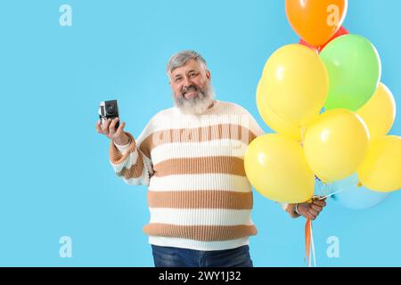 Senior Mann mit Ballons und Fotokamera auf blauem Hintergrund Stockfoto