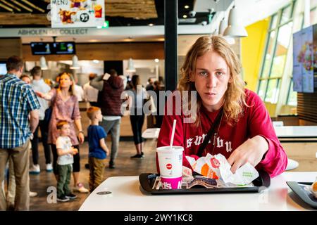 Lucas V / Leonard W Berlin, Deutschland. Junger Erwachsener, männlicher Musikschüler, der während seiner Mittagspause im McDonalds Fastfood Restaurant ungesunde Hamburger isst. MRYES Berlin Bahnhof Zoo / MacDonalds Berlin Deutschland Copyright: XGuidoxKoppesx Stockfoto