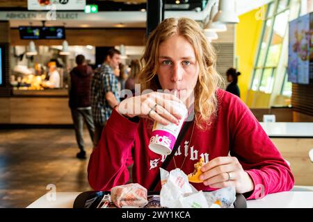 Lucas V / Leonard W Berlin, Deutschland. Junger Erwachsener, männlicher Musikschüler, der während seiner Mittagspause im McDonalds Fastfood Restaurant ungesunde Hamburger isst. MRYES Berlin Bahnhof Zoo / MacDonalds Berlin Deutschland Copyright: XGuidoxKoppesx Stockfoto