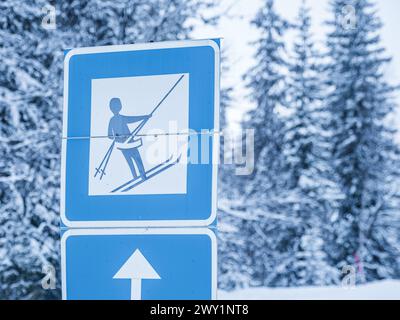 Ein blau-weißes Skilift-Straßenschild steht vor dem Hintergrund schneebedeckter Bäume in Schweden, das die Skifahrer zu den nahe gelegenen Liften unter einem W führt Stockfoto