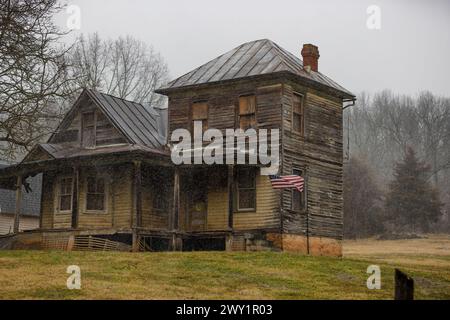 Stokesville, Virginia, USA - Sitzen vernachlässigt in diesem alten Haus hängt bei regnerischem Wetter eine amerikanische Flagge von seiner Veranda. Stockfoto