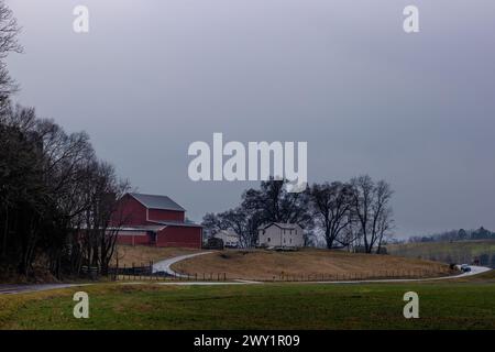 Staunton, Virginia, USA – 25. Februar 2024: Eine Straße führt um diesen kleinen Hügel, in dem sich ein Bauernhaus und eine Scheune im ländlichen Virginia befinden. Stockfoto