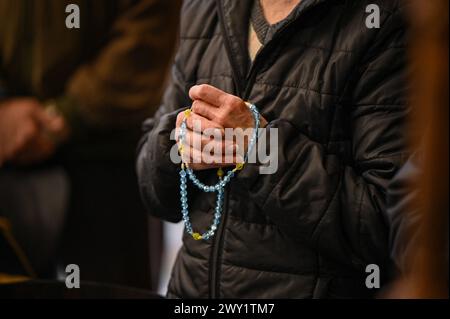 LEMBERG, UKRAINE - 3. APRIL 2024 - Eine ältere Frau hält während eines gemeinsamen Gebets in der Garnisonskirche der Heiligen Peter und Paul Perlen in den Nationalfarben im Rahmen der Feier zum 34. Jahrestag des Hissens der ukrainischen Flagge über dem Rathaus von Lemberg, Lwiw, Westukraine. Stockfoto