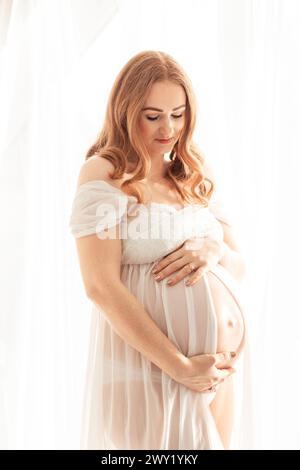 Schöne rothaarige schwangere Frau mittleren Alters, die zu Hause ein Baby erwartet Stockfoto