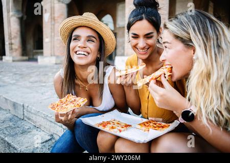 Drei fröhliche Frauen, die Spaß beim Pizza-Essen in Italien haben Stockfoto
