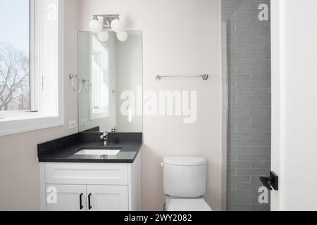 Badezimmer mit weißem Schrank, schwarzer Marmorplatte und Dusche mit grauen U-Bahn-Fliesen. Stockfoto