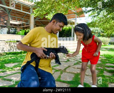 Ein wunderbares Bild eines indischen Vaters und seiner Tochter, die glückliche Erinnerungen beim Spielen mit einer jungen Ziege schaffen Stockfoto