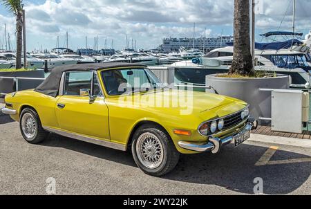 Ein gelber zweisitziger, verdeckter Triumph-Hirsch am Kai in Vilamoua, Portugal. Hergestellt von British Leyland. Stockfoto