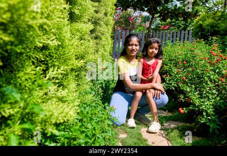 Ein herzerwärmendes Bild einer Mutter und ihrer Tochter, die zusammen in einem lebendigen Garten sitzen und ein Lächeln auf die Kamera strahlen Stockfoto