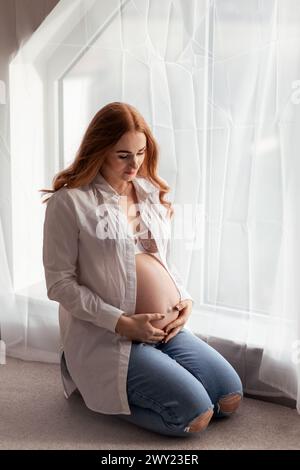 Schöne rothaarige schwangere Frau mittleren Alters, die zu Hause ein Baby erwartet Stockfoto