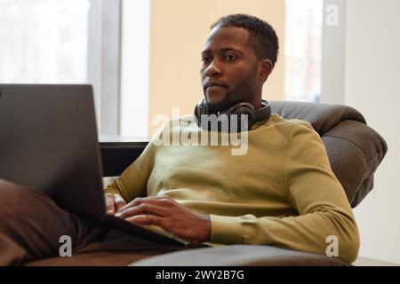 Sauberes Porträt eines jungen afroamerikanischen Mannes, der einen Laptop benutzte und in der Bürolounge arbeitete Stockfoto