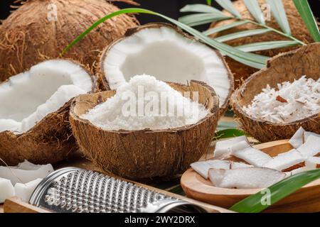 Frisch geöffnete Kokosnüsse zusammen mit Kokosscheiben, Flocken und Kokosblättern auf einem Holztisch. Schöner Hintergrund für Ihre Projekte. Stockfoto