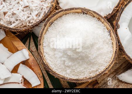 Frisch geöffnete Kokosnüsse zusammen mit Kokosscheiben, Flocken und Kokosblättern auf einem Holztisch. Schöner Hintergrund für Ihre Projekte. Stockfoto