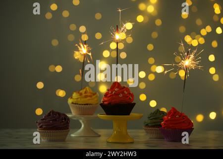 Verschiedene bunte Cupcakes mit Glitzern auf dem Tisch gegen verschwommenes Licht Stockfoto