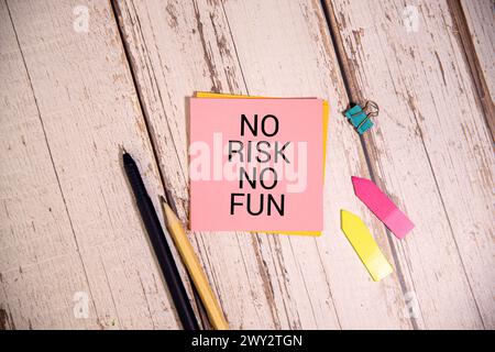 Gelber selbstklebender Notizaufkleber diagonal auf einer dunklen Holztischplatte mit stilisierter Handschrift mit dem Text: Kein Risiko kein Spaß Stockfoto