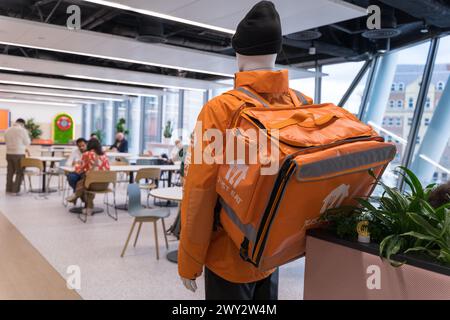 Rückansicht eines Fastfood-Liefermannes, der in Orange gekleidet war, in einer Just Eat Jacke und einem orangen Rucksack, ging in die Personalkantine, London England Stockfoto