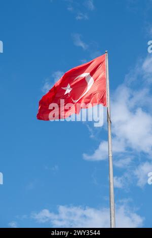 Flagge der Republik Türkei auf einem Fahnenmast, der sich im Wind gegen den blauen Himmel öffnet Stockfoto