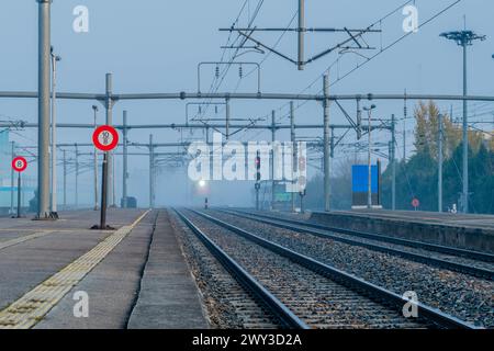 Leerer Bahnsteig an einem Bahnhof an einem nebeligen Tag mit elektrischer Ausrüstung über der Decke und Licht des sich nähernden Zuges in Südkorea Stockfoto