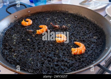 Schwarzer Reis mit Garnelen und Tintenfisch, ein trockener Reis, der in Paella oder in einem Tontopf gekocht wird, ein charakteristischer Geschmack der valencianischen mediterranen Küche. Spanien Stockfoto