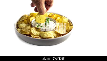 Die Hand des Mannes hält Kartoffelknusprig und taucht sie in Sauerrahm und Schnittlauch-Dip isoliert auf weiß Stockfoto