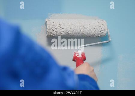 Nahaufnahme einer Frau, die die Wand ihres Hauses mit einer Walze malte, in einer helleren Farbe als die alte Stockfoto