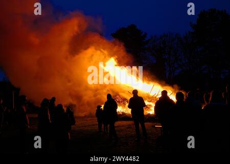 Uelsen, Deutschland März 31 2024 Silhouetten von Menschen, die auf ein riesiges Osterfeuer blicken. Dies ist eine festliche Veranstaltung in vielen deutschen Dörfern Stockfoto