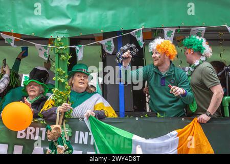 Menschen, die auf einem Wagen lachen und singen, nehmen an der Prozession bei der St. Patrick's Day Parade in London Teil. St. Patrick's Day. Stockfoto