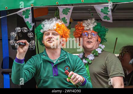 Freunde in dreifarbigen Perücken lachen und singen auf einem Wagen, der an der Prozession bei der St. Patrick's Day Parade in London teilnimmt. St. Patrick's Day. Stockfoto