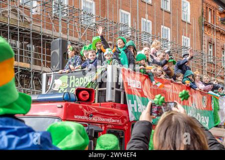 Die London Fire Brigades Emerald Society kommt während der Prozession bei der St. Patrick's Day Parade in London an den Menschenmassen auf einem Feuerwehrauto vorbei. Stockfoto