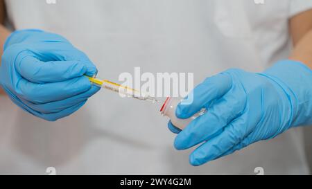 Eine Person, die blaue Handschuhe trägt, hält ein Thermometer und eine Spritze in der Hand. Die Person bereitet sich darauf vor, einen Schuss zu geben Stockfoto