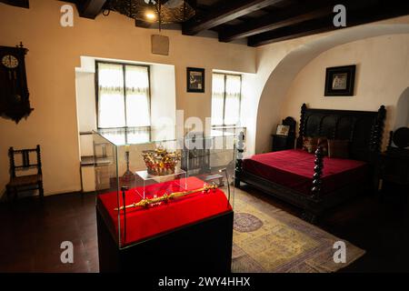 Bran, Brasov, Rumänien – Juni 2023: Klassisches Vintage-Schlafzimmer mit luxuriöser Krone in einem Glaskoffer, antiken Möbeln und warmer Sonnenlichtfilterin Stockfoto
