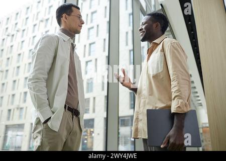 Niedrigwinkelporträt zweier stilvoller junger Männer, die bei der Arbeit am Fenster plaudern Stockfoto