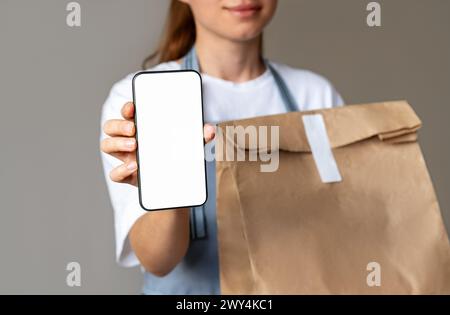 Mockup Mobile App für die Lieferung von Lebensmitteln. Online-Bestellung zum Mitnehmen. Handys- und Papiertüte mit Essen zum Mitnehmen in den Händen der Kellnerin. Take-HOM Stockfoto