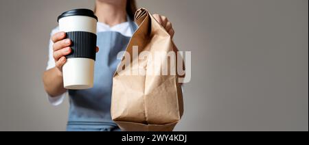 Die Kellnerin gibt Essen zum Mitnehmen, Kaffeetasse und braune Papiertüte in den Händen. Stockfoto