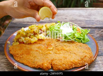 Eine Zitronenscheibe mit der Hand auf das frisch gebratene Schnitzel drücken Stockfoto