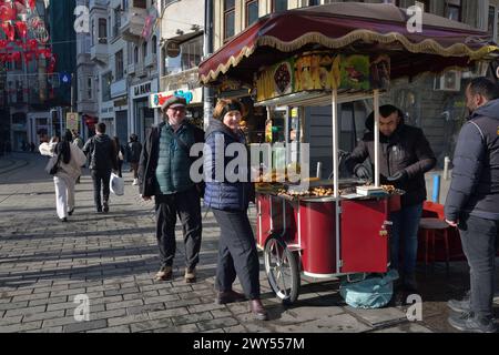 Istanbul, Türkei - 10. Dezember 2023: Glückliches Touristenpaar Bucht geröstete Kastanien auf der Itiklal Straße in Istanbul an einem sonnigen Wintertag in der Türkei. Traditi Stockfoto